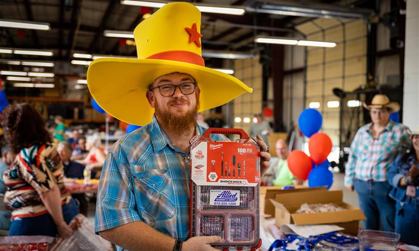 A man wearing a large yellow cowboy hat holds up a toolkit